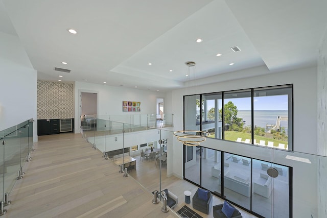 interior space with a water view, a raised ceiling, and light wood-type flooring