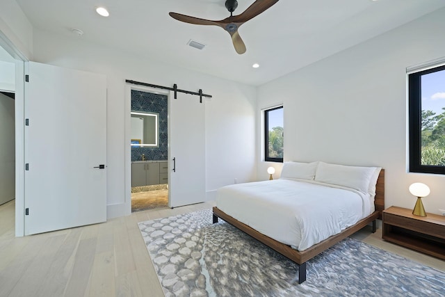 bedroom with multiple windows, ceiling fan, a barn door, and light wood-type flooring