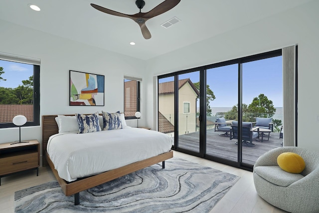 bedroom featuring multiple windows, a water view, access to outside, and light wood-type flooring