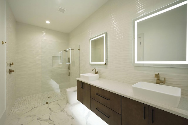 bathroom featuring a tile shower, vanity, tile walls, and toilet