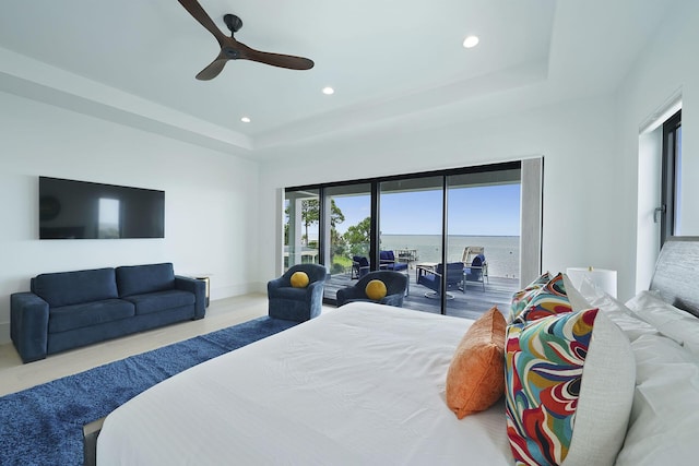 bedroom featuring a tray ceiling, access to outside, ceiling fan, and a water view