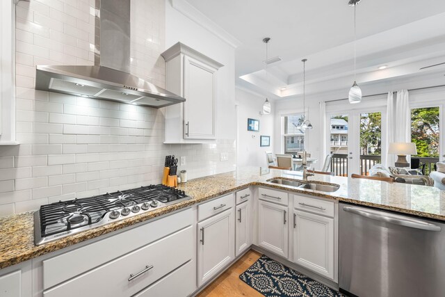 kitchen with appliances with stainless steel finishes, white cabinetry, light stone counters, decorative light fixtures, and wall chimney exhaust hood