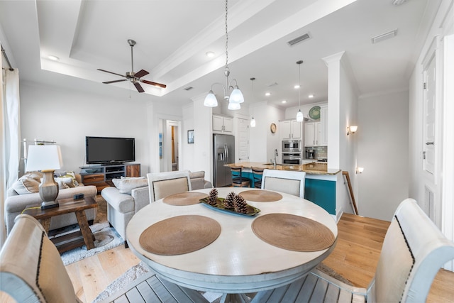 dining space featuring ceiling fan with notable chandelier, ornamental molding, a tray ceiling, and light hardwood / wood-style floors