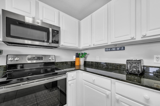 kitchen featuring dark stone countertops, stainless steel appliances, and white cabinets