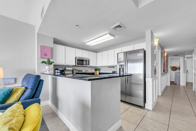 kitchen with appliances with stainless steel finishes, light tile patterned floors, white cabinets, and kitchen peninsula