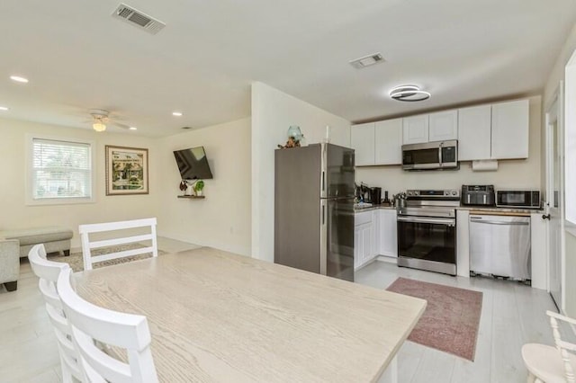 kitchen featuring white cabinets, visible vents, stainless steel appliances, and open floor plan