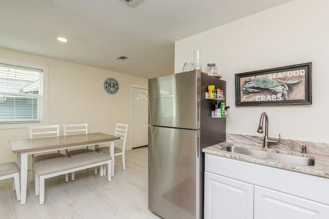 kitchen with white cabinets, light wood-style flooring, light stone counters, freestanding refrigerator, and a sink