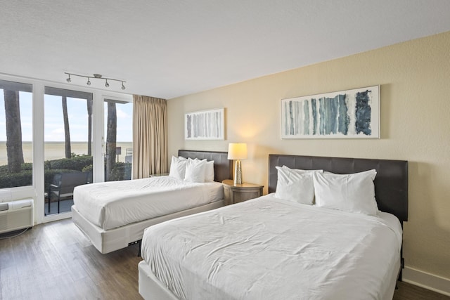 bedroom with a water view, dark wood-type flooring, access to exterior, and track lighting