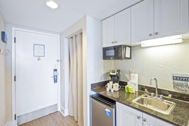 kitchen with dark stone countertops, sink, stainless steel fridge, and white cabinets