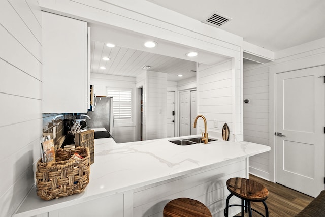 kitchen with sink, a breakfast bar area, white cabinets, light stone counters, and kitchen peninsula