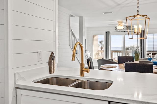 kitchen featuring sink, white cabinetry, light stone counters, a notable chandelier, and decorative light fixtures