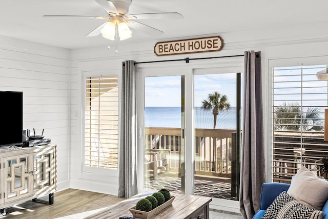 doorway to outside featuring a water view, ceiling fan, wooden walls, and light hardwood / wood-style flooring