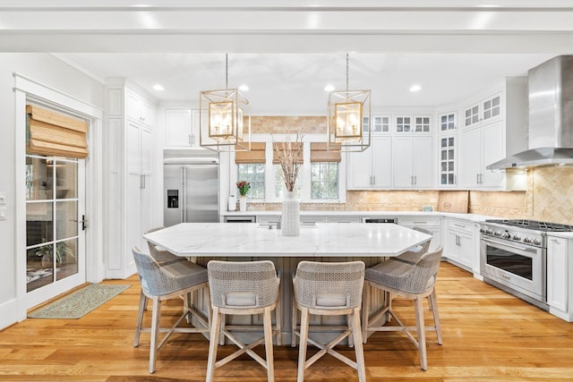 kitchen with decorative backsplash, white cabinets, premium appliances, wall chimney exhaust hood, and a center island