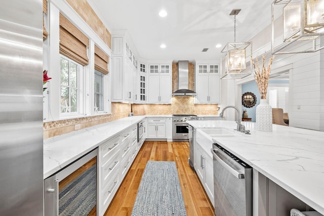 kitchen featuring wine cooler, stainless steel appliances, a sink, light wood-style floors, and wall chimney range hood