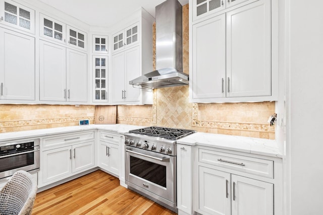 kitchen with tasteful backsplash, wall chimney range hood, appliances with stainless steel finishes, and white cabinetry