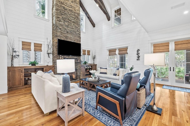 living room featuring french doors, beamed ceiling, a stone fireplace, and light wood finished floors