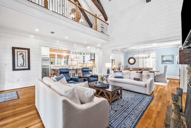 living area featuring beam ceiling, a high ceiling, light wood-style flooring, and a notable chandelier