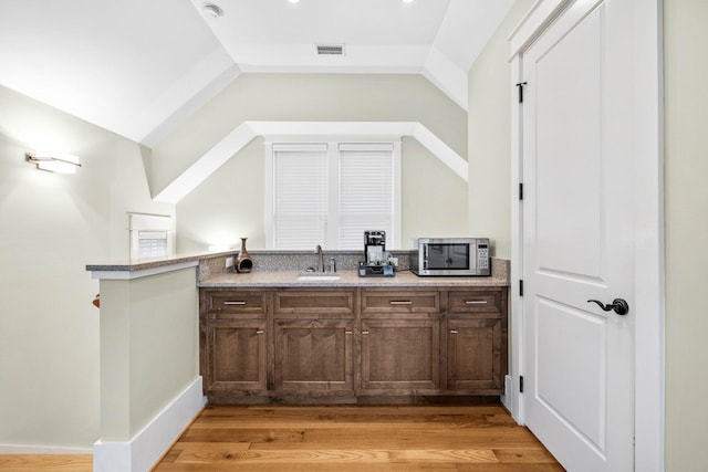 bar with lofted ceiling, visible vents, stainless steel microwave, a sink, and light wood-type flooring