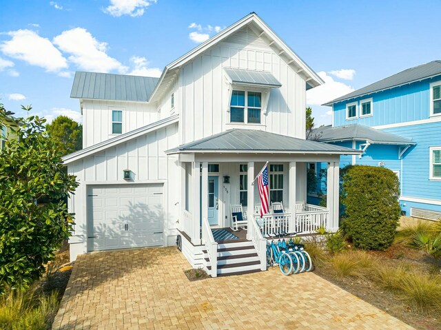 modern farmhouse with decorative driveway, covered porch, board and batten siding, metal roof, and a garage