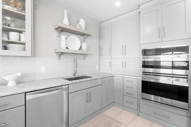 kitchen featuring sink, tasteful backsplash, light tile patterned floors, stainless steel appliances, and light stone countertops