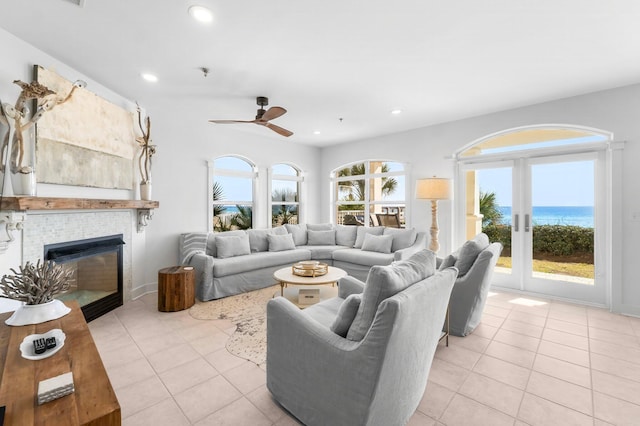 living room with a water view, light tile patterned flooring, a tile fireplace, and french doors