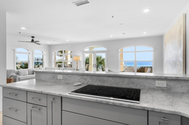 kitchen with light stone countertops, gray cabinetry, black electric stovetop, and ceiling fan