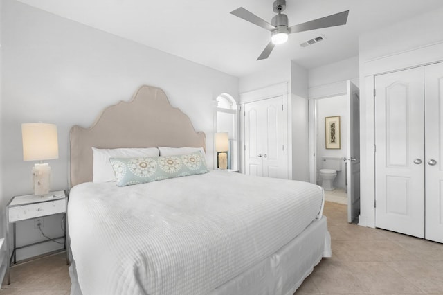 tiled bedroom with multiple closets, ceiling fan, and ensuite bath