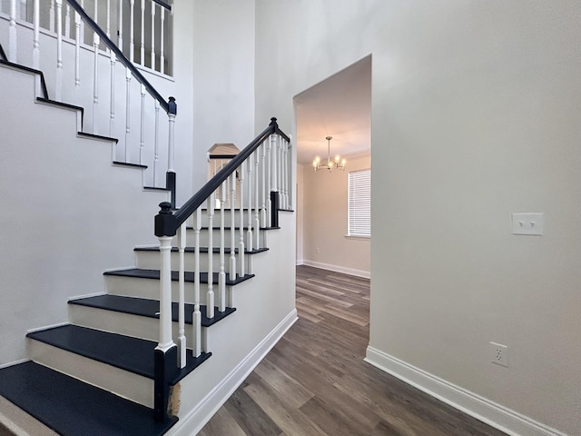 stairway with a towering ceiling, wood-type flooring, and a chandelier