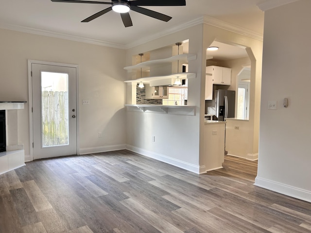 unfurnished living room with ceiling fan, ornamental molding, and light wood-type flooring