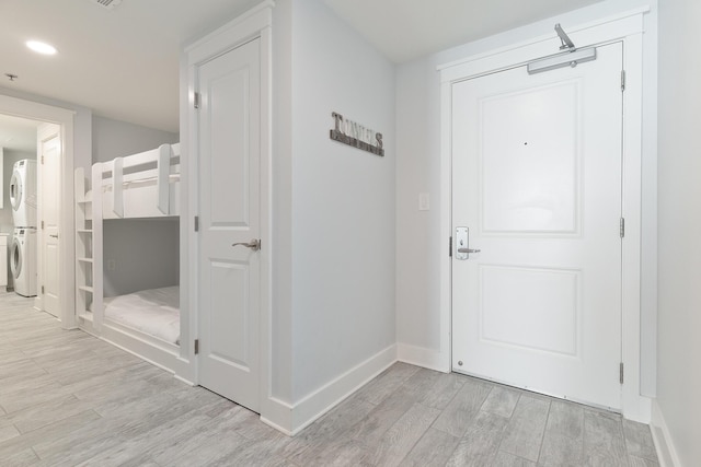 corridor with stacked washer / drying machine and light hardwood / wood-style flooring