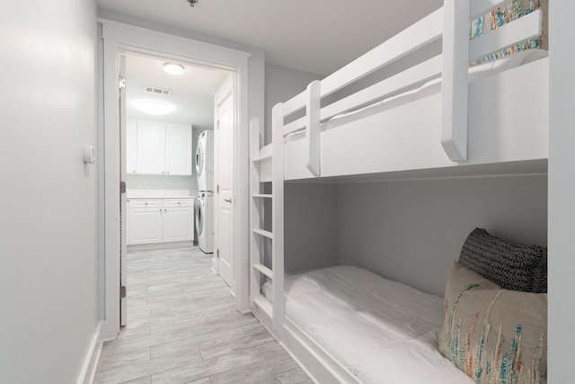 bedroom featuring stacked washer and dryer, ensuite bath, and light hardwood / wood-style flooring