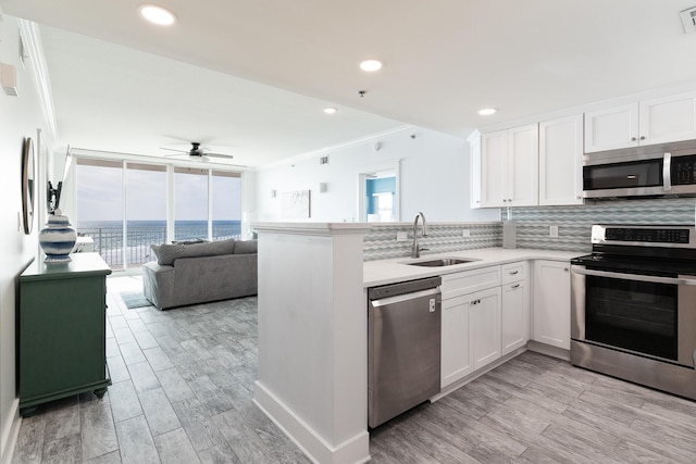 kitchen with sink, a water view, appliances with stainless steel finishes, decorative backsplash, and white cabinets