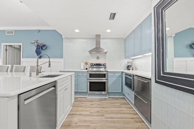 kitchen with sink, ornamental molding, wall chimney exhaust hood, stainless steel appliances, and light hardwood / wood-style flooring