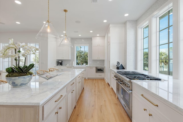 kitchen with a spacious island, white cabinets, high end stainless steel range, light stone counters, and light hardwood / wood-style flooring