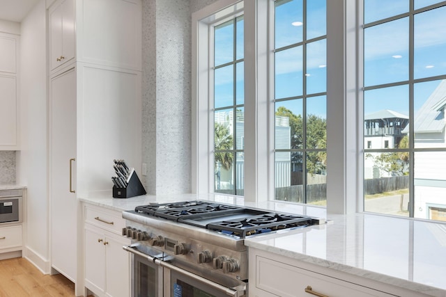 kitchen with white cabinets, decorative backsplash, range with two ovens, light stone counters, and light hardwood / wood-style flooring