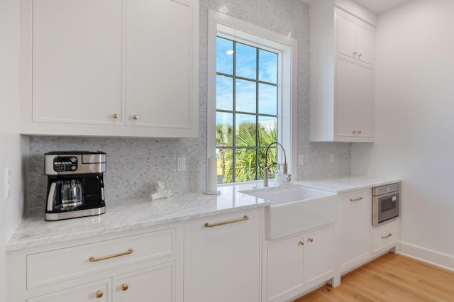 kitchen featuring sink, light hardwood / wood-style flooring, light stone countertops, and white cabinets