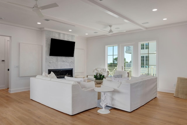 living room with a fireplace, beamed ceiling, ceiling fan, light hardwood / wood-style floors, and crown molding