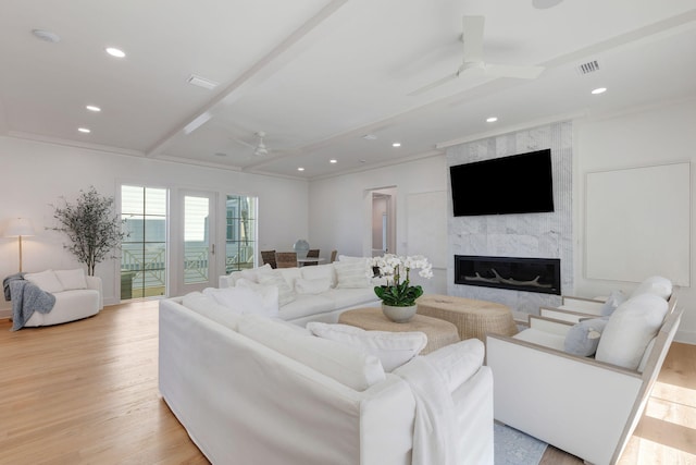 living room featuring beamed ceiling, ceiling fan, a high end fireplace, light hardwood / wood-style floors, and crown molding