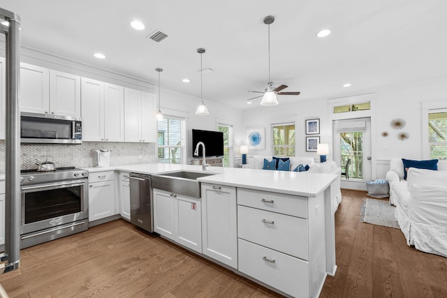 kitchen with sink, appliances with stainless steel finishes, white cabinets, and hanging light fixtures