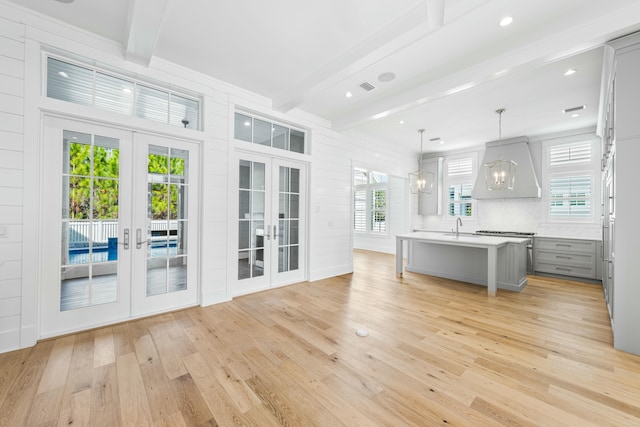 kitchen featuring french doors, a center island with sink, gray cabinets, light countertops, and hanging light fixtures