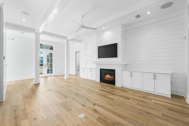 unfurnished living room with wood walls, beamed ceiling, light hardwood / wood-style flooring, ceiling fan, and french doors