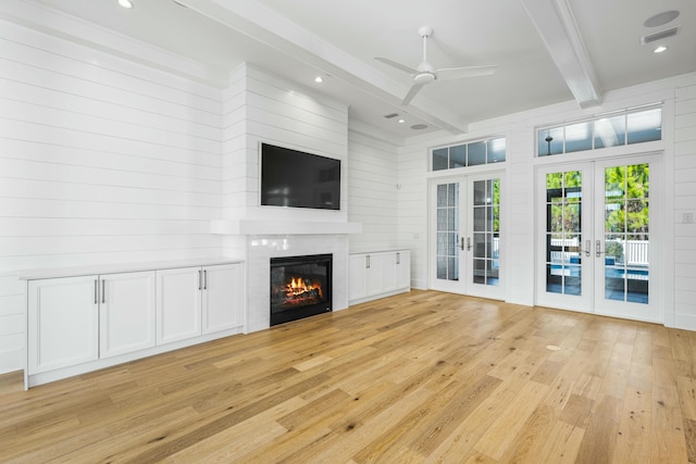 unfurnished living room with french doors, wooden walls, ceiling fan, beam ceiling, and light hardwood / wood-style floors