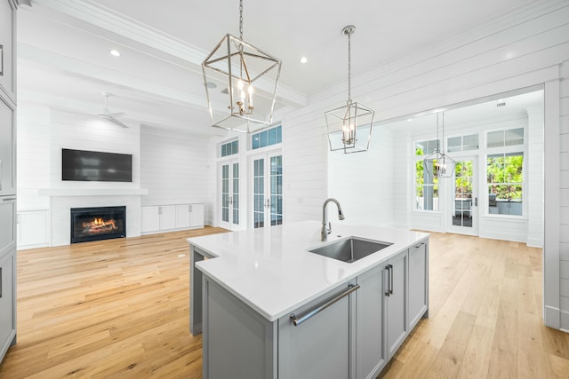 kitchen with decorative light fixtures, gray cabinets, light countertops, a sink, and an island with sink