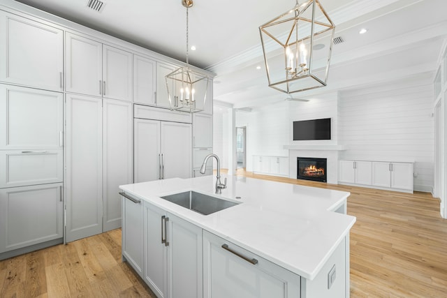 kitchen with sink, pendant lighting, a kitchen island with sink, and light hardwood / wood-style flooring