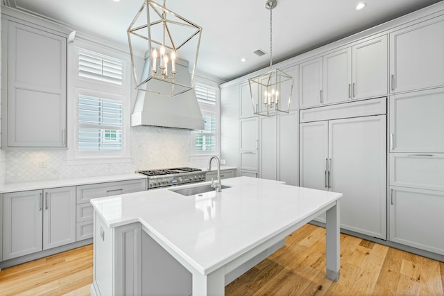 kitchen featuring a kitchen island with sink, light countertops, a sink, and decorative light fixtures