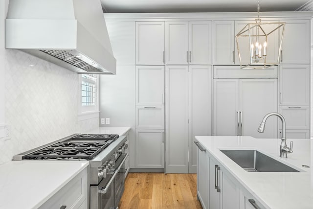 kitchen featuring sink, premium range hood, hanging light fixtures, high quality appliances, and light hardwood / wood-style floors