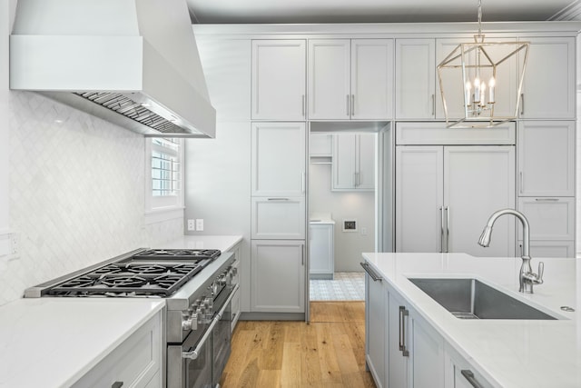 kitchen with premium appliances, light wood-style flooring, premium range hood, a sink, and hanging light fixtures