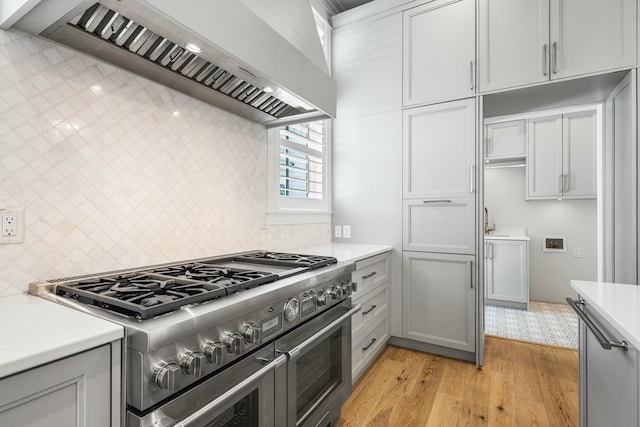 kitchen with light wood finished floors, wall chimney exhaust hood, light countertops, double oven range, and backsplash