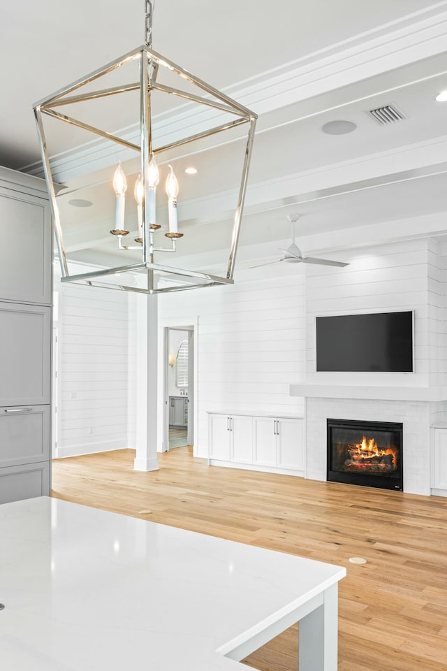 unfurnished living room with hardwood / wood-style flooring, beam ceiling, and ceiling fan with notable chandelier