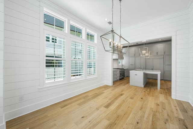 unfurnished dining area with an inviting chandelier, wood walls, sink, ornamental molding, and light wood-type flooring